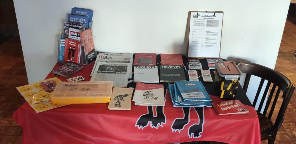 Ein Tisch, auf dem veschiedene Broschüren und Zeitschriften ausliegen. Links steht ein kleiner Flyerständer.